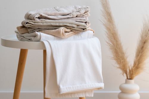 Une pile de vêtements neutres pliés sur une table blanche