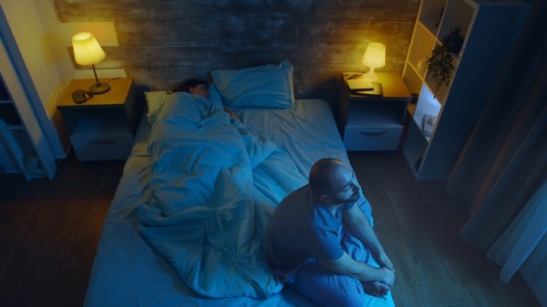 un homme assis sur son lit, pendant la nuit